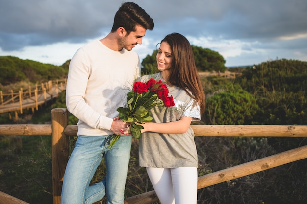 Foto gratuita pareja apoyada en una barandilla de un puente con un ramo de rosas