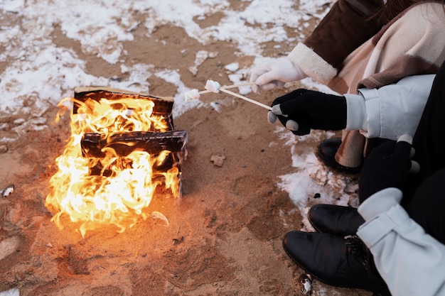 Pareja asando malvaviscos en el fuego durante un viaje de invierno en la playa