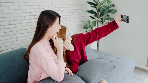 Pareja asiática lesbiana usando teléfono inteligente selfie en sala de estar en casa