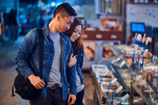 Pareja asiática romántica que busca algo especial en el mercado chainese de mariscos. Son curiosos y alegres.