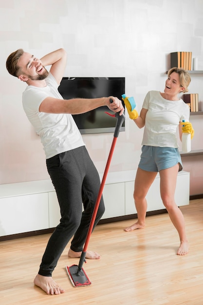 Pareja bailando en el interior con productos de limpieza