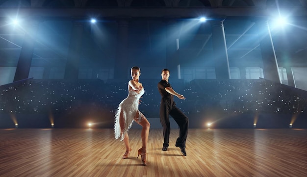 Pareja de bailarines realizan bailes latinos en un gran escenario profesional