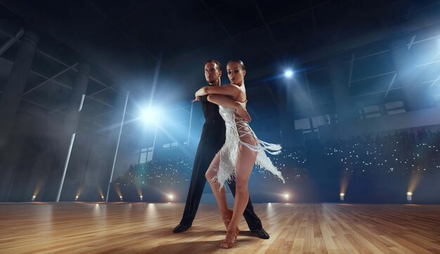 Pareja de bailarines realizan bailes latinos en un gran escenario profesional