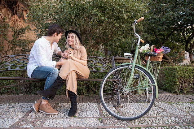 Pareja en el banco con bicicleta y flores.