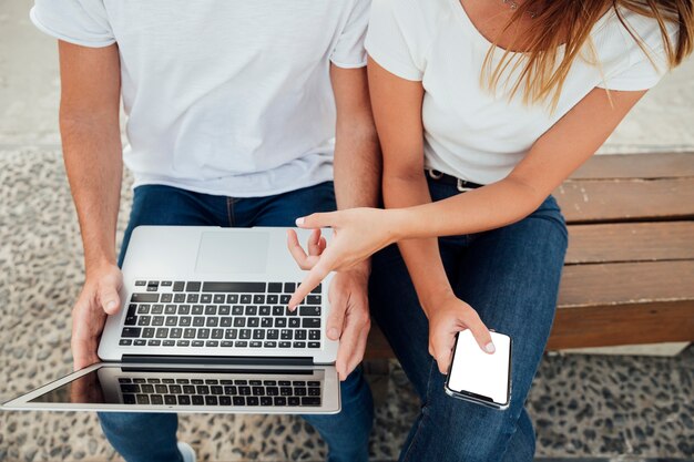 Pareja en un banco con teléfono y computadora portátil