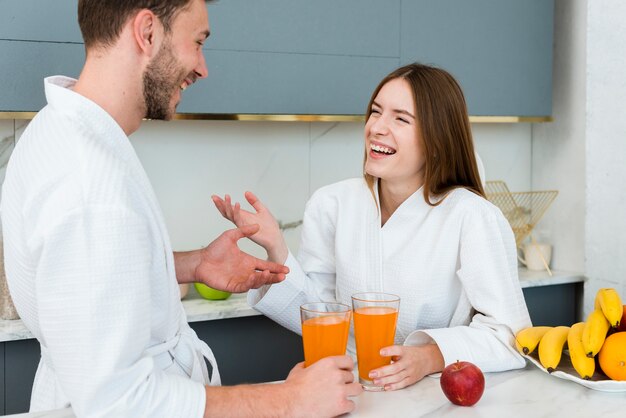 Pareja en batas de baño disfrutando de jugo en la cocina