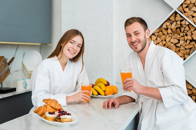 Pareja en batas de baño posando con vasos de jugo