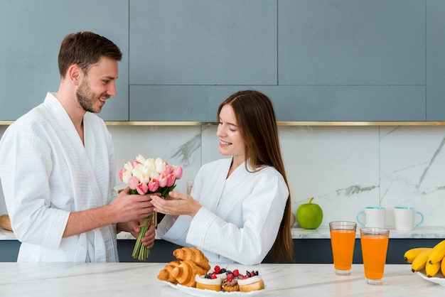 Pareja en batas de baño sonriendo y sosteniendo ramo de tulipanes