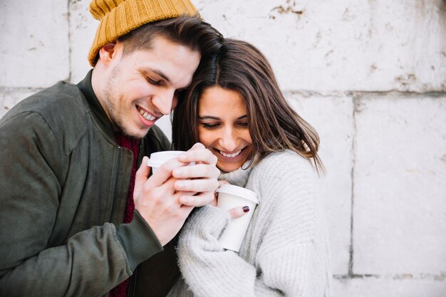 Pareja con bebidas calientes calentando las manos