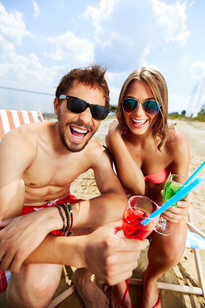 Pareja bebiendo y riendo en la playa