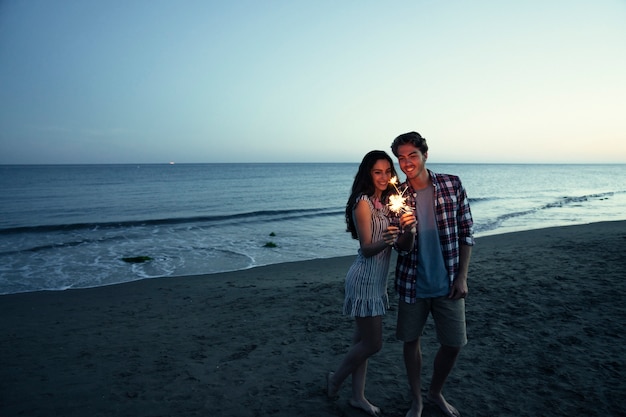 Foto gratuita pareja con bengala en una playa de atardecer