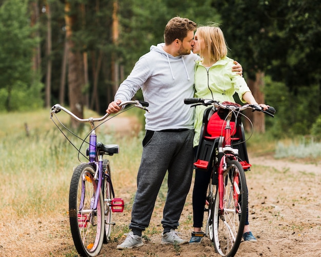 Foto gratuita pareja besándose al lado de bicicletas en camino forestal