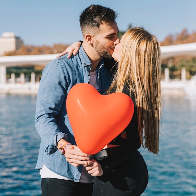 Pareja besándose alegre con globo de corazón