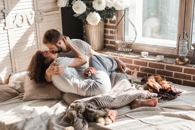 Pareja besándose en la cama desordenada