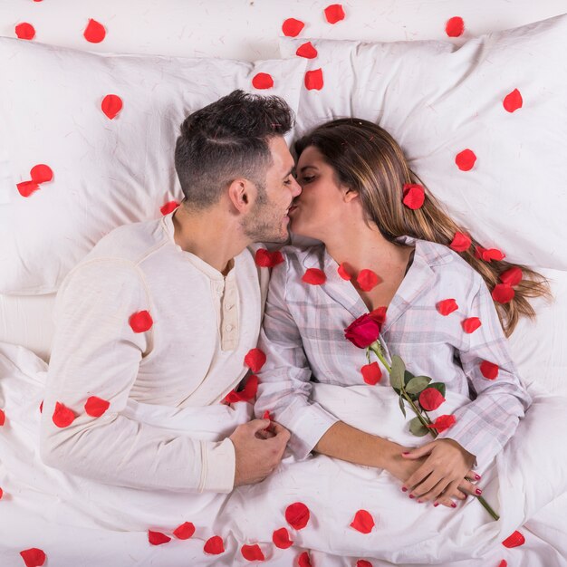 Pareja besándose en la cama con pétalos de rosa