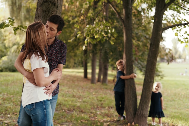 Pareja besándose mientras sus hijos miran al aire libre