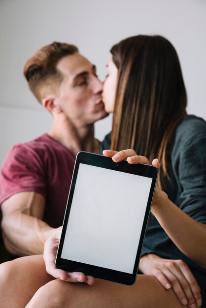 Pareja besándose y mostrando tableta con pantalla en blanco