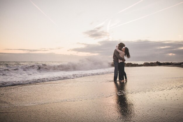 Pareja besándose en la orilla de la playa al atardecer