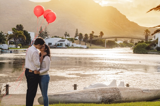 Pareja besándose en un parque con globos rojos al atardecer