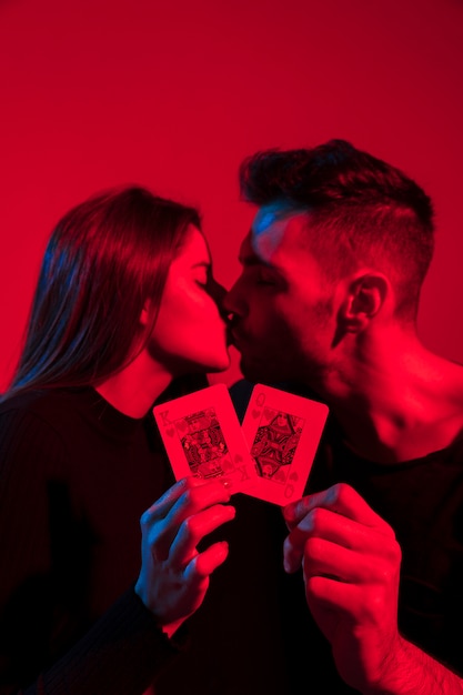 Foto gratuita pareja besándose y sosteniendo rey y reina de corazones jugando a las cartas