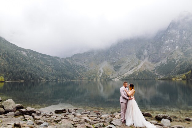 Pareja de boda romántica en pie de amor del lago Sea Eye en Polonia. Montes Tatra.