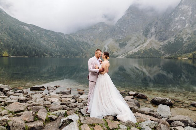 Pareja de boda romántica en pie de amor del lago Sea Eye en Polonia. Montes Tatra.