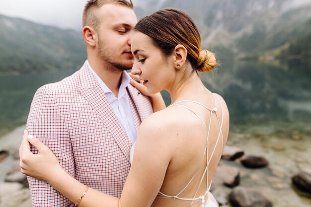 Pareja de boda romántica en pie de amor del lago Sea Eye en Polonia. Montes Tatra.