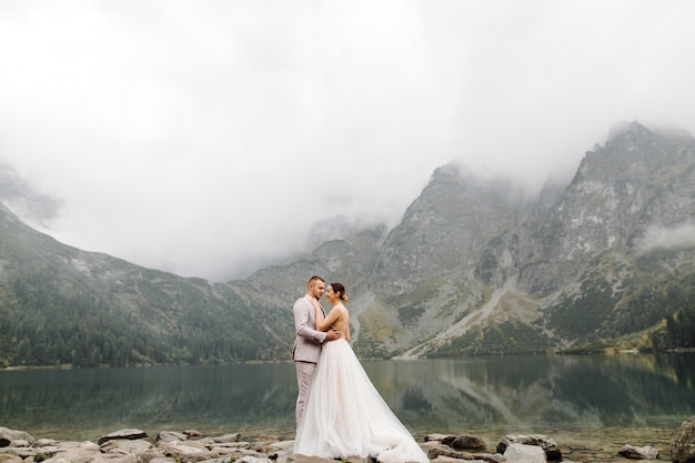 Pareja de boda romántica en pie de amor del lago Sea Eye en Polonia. Montes Tatra.