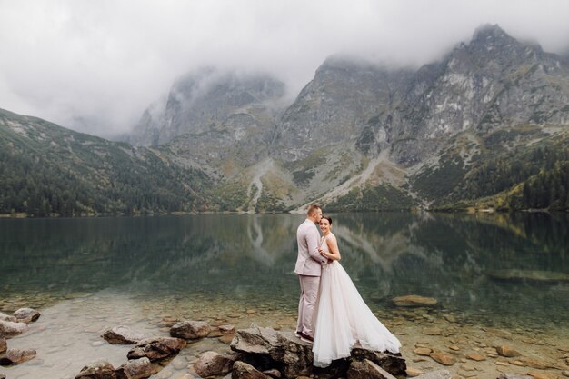 Pareja de boda romántica en pie de amor del lago Sea Eye en Polonia. Montes Tatra.