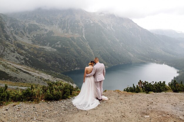 Pareja de boda romántica en pie de amor del lago Sea Eye en Polonia. Montes Tatra.