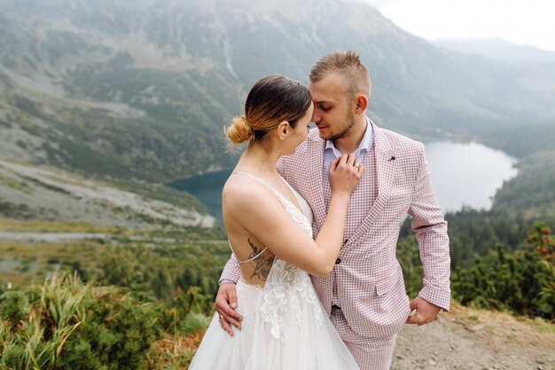 Pareja de boda romántica en pie de amor del lago Sea Eye en Polonia. Montes Tatra.