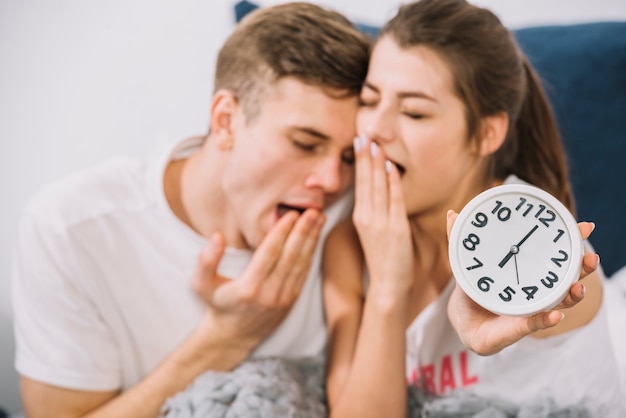 Foto gratuita pareja bostezando en la cama mostrando el reloj a las 6 am