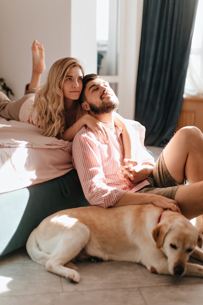 Pareja de buen humor disfruta de un fin de semana relajado. Chico y chica se divierten con su perro en el dormitorio.