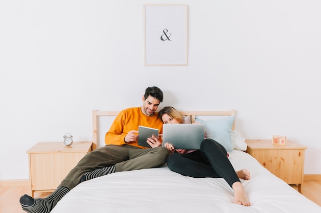 Pareja en la cama usando tecnologías