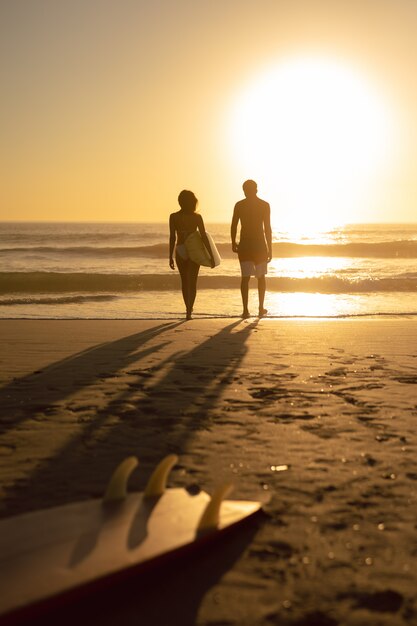 Pareja caminando junto con tabla de surf en la playa