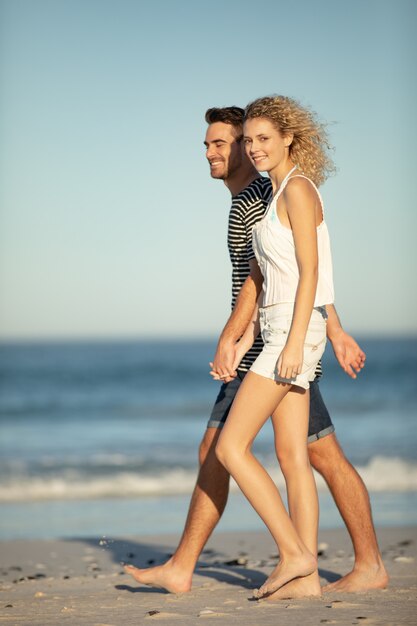 Pareja caminando juntos de la mano en la playa