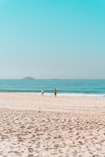 Pareja caminando por la orilla de una playa soleada con un cielo despejado arriba