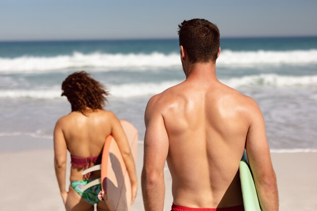 Pareja caminando con tabla de surf en la playa bajo el sol