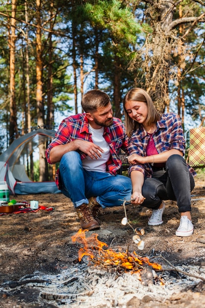 Pareja en camping cocinando marshmellow en llamas