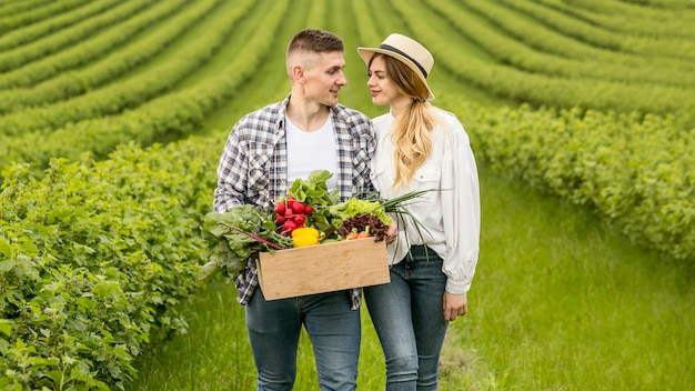 Pareja con canasta de verduras en tierras de cultivo