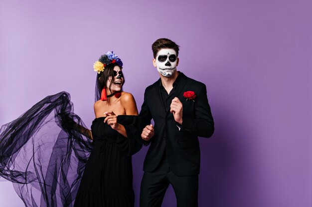 Pareja con caras pintadas colgando. Foto de niña morena en imagen de novia y su novio en traje clásico.