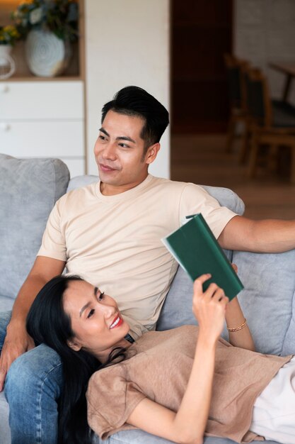 Pareja cariñosa en casa en el sofá leyendo un libro y tomando una copa