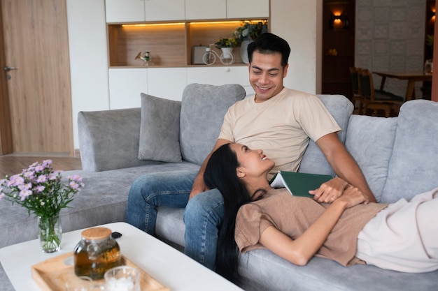 Pareja cariñosa en casa en el sofá leyendo un libro y tomando una copa