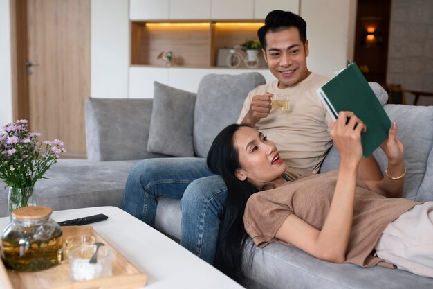 Pareja cariñosa en casa en el sofá leyendo un libro y tomando una copa