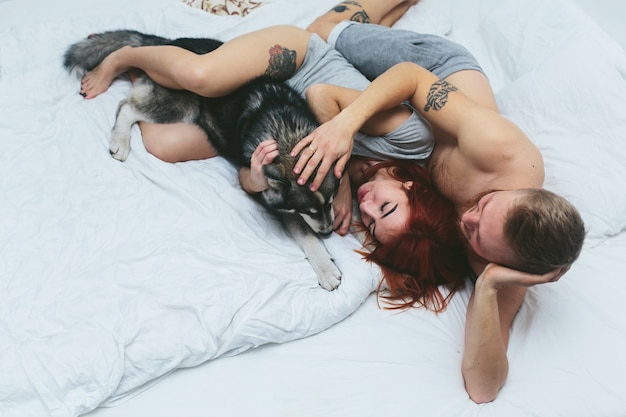 Pareja cariñosa jugando con el perro en la cama