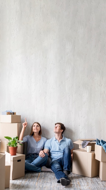 Pareja en casa empacando para mudarse y apuntando hacia arriba