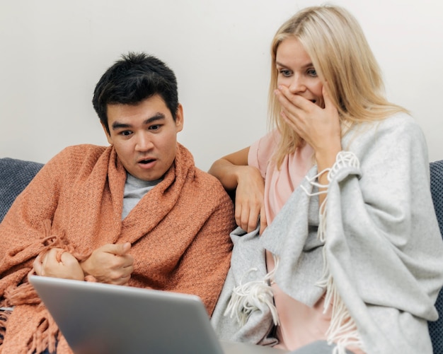 Pareja en casa juntos mirando asombrado por portátil