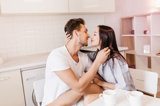 Pareja casada besándose durante el desayuno en la acogedora habitación blanca