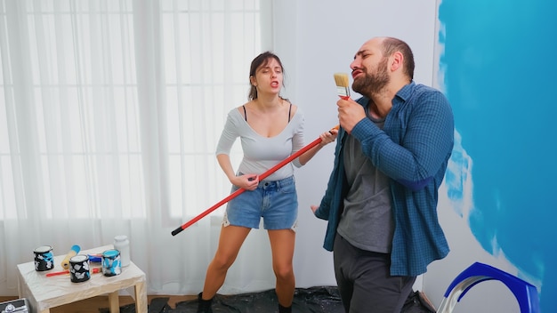 Pareja casada cantando sobre herramientas de renovación bañadas en pintura azul. Pareja casada alegre durante el cambio de imagen de la casa. Decoración y renovación del hogar en acogedor piso, reparación y renovación.