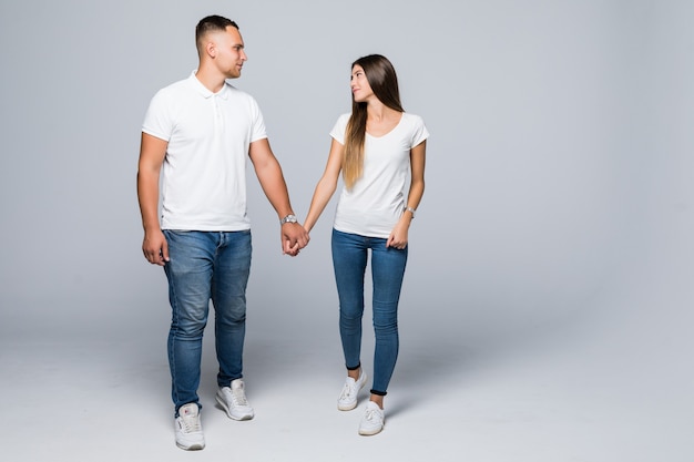 Pareja casual está caminando hacia la cámara mirando el uno al otro aislado en la pared blanca